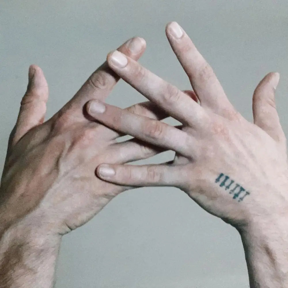 Two interlocked human hands with a small tattoo on the right hand.